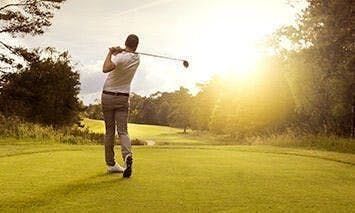 man hitting golf ball into sunset